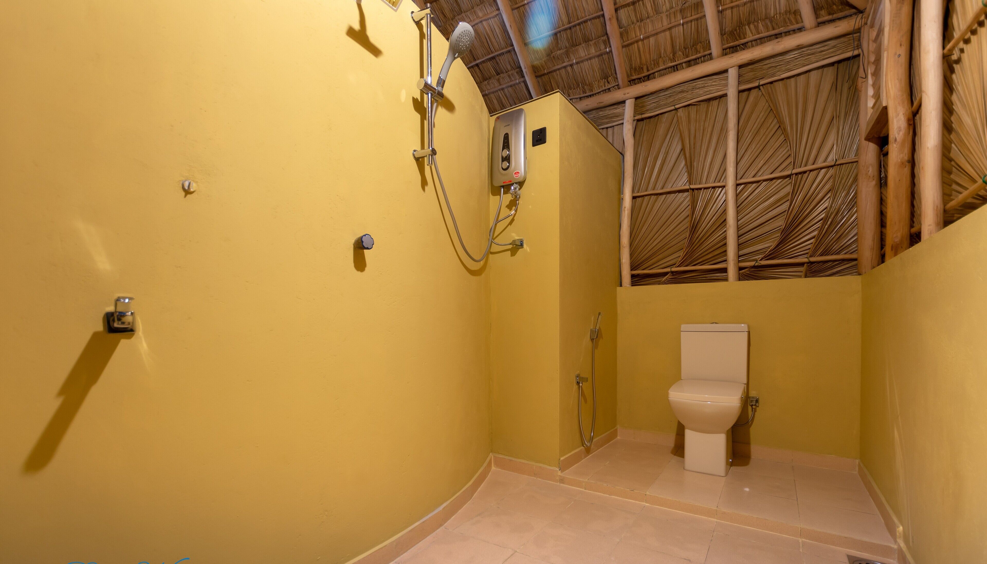 A small, yellow-walled bathroom with a bamboo ceiling, a toilet, and a shower with a handheld showerhead.