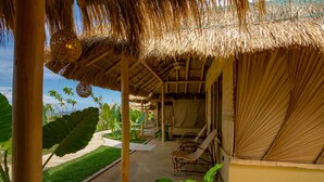 A thatched-roof outdoor seating area with lounge chairs, surrounded by tropical plants and a clear view of the ocean. - Blue Waters Arugambay (Pottuvil)