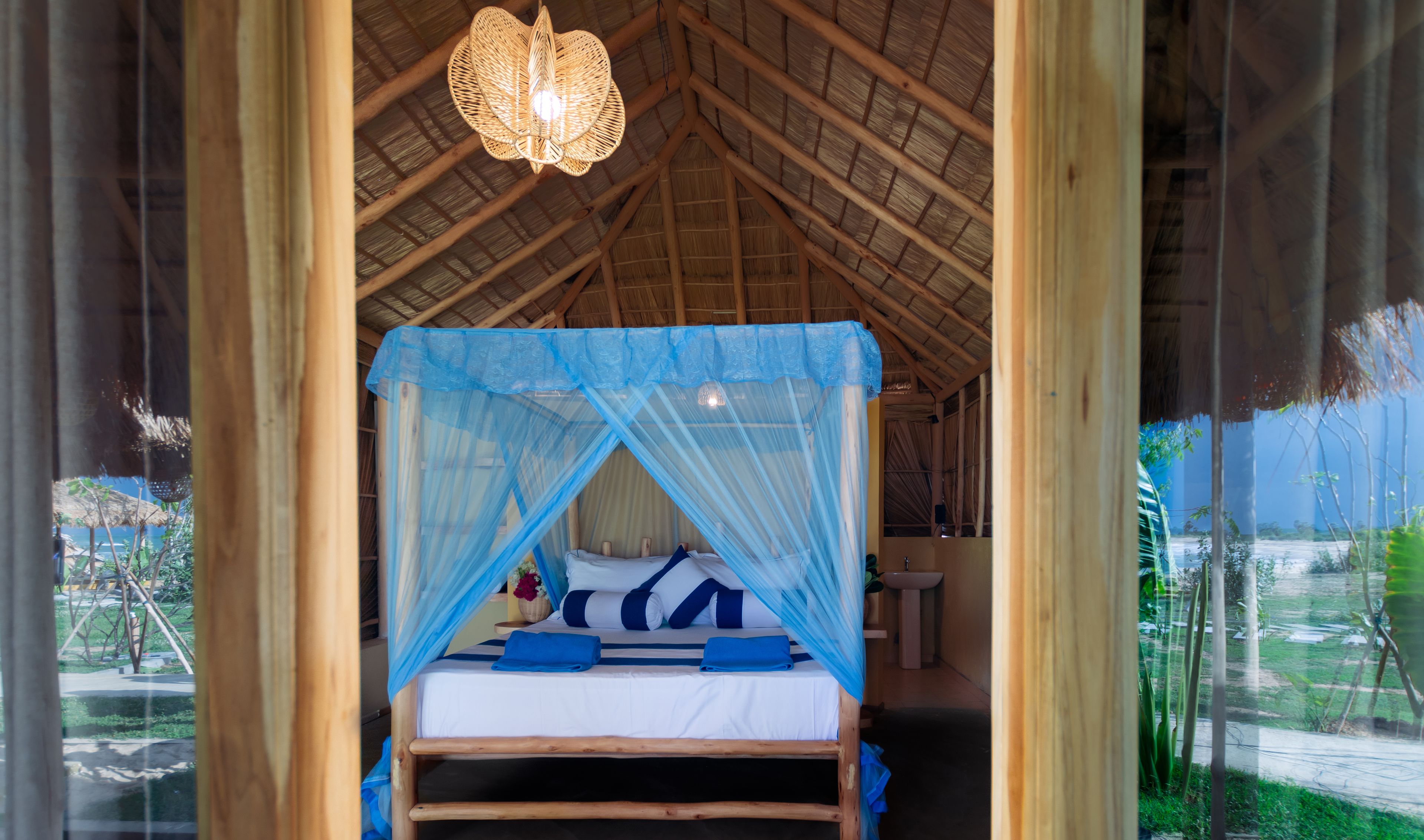 Una habitación con una cama bajo un dosel azul, vigas de madera en el techo y una lámpara colgante.