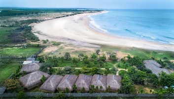 Un resort en la playa con cabañas de techo de paja, una playa arenosa y vista al océano.