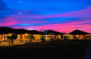 Un resort con cabañas de techo de paja, cielo nocturno despejado y un camino que lleva a las construcciones.