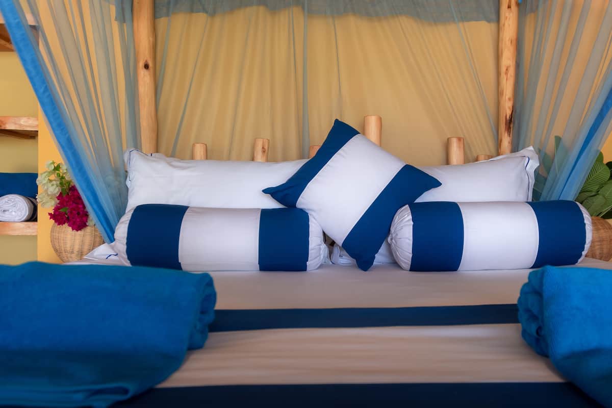 A bed with blue and white striped pillows, a canopy, and a wicker basket with flowers.