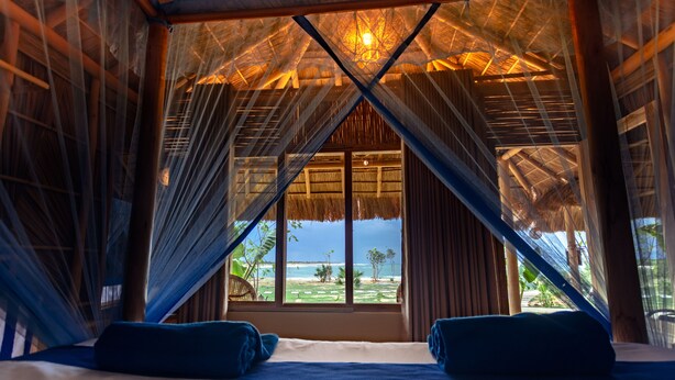 A room with a thatched roof, a large window, and a view of the beach. - Blue Waters Arugambay (Pottuvil)