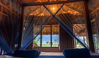 Una habitación con techo de paja, un ventanal y vista a la playa.