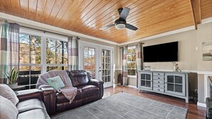 A living room with a leather sofa, a gray rug, a ceiling fan, and a TV on a cabinet. - Perfect lakefront house in quite cove! Walking distance to Mt Lake Marina. <br> (Rocky Top)