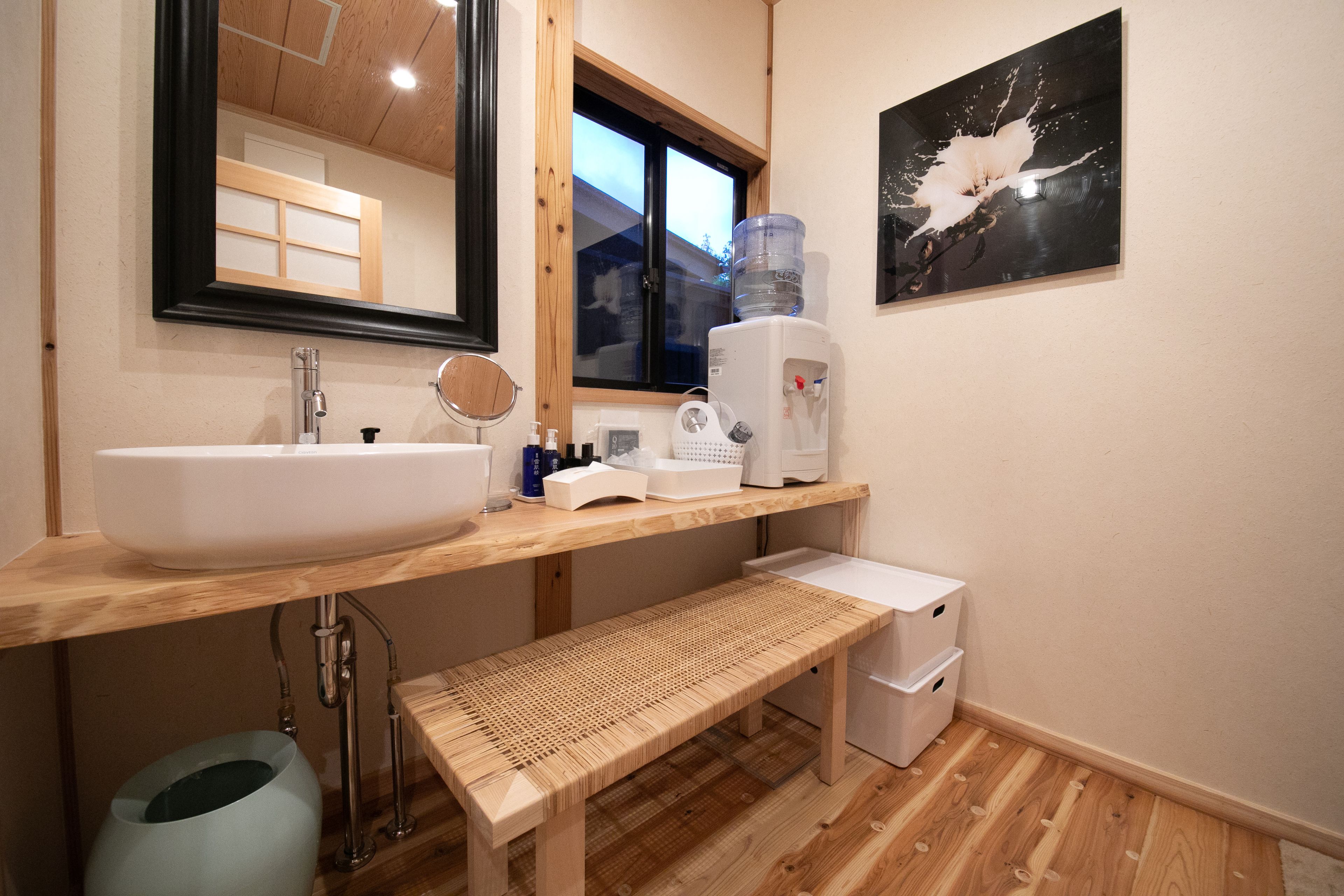 A bathroom with a wooden vanity, a large mirror, a sink, a water dispenser, and a bench.
