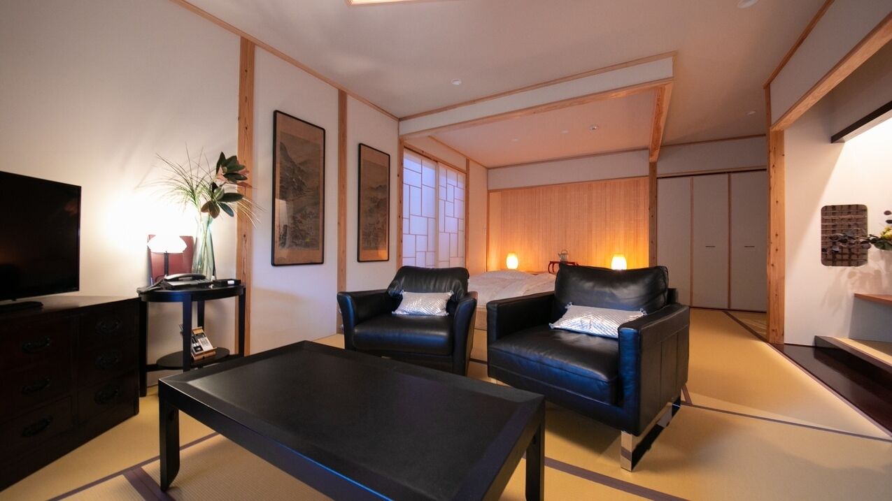 Ein modernes Wohnzimmer mit einer Couch, Sesseln, einem Couchtisch, einem Fernseher und einer Zierpflanze.