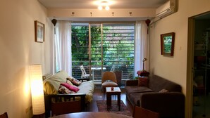 Ein gemütliches Wohnzimmer mit einem Esstisch, Sofas und einem großen Fenster mit Blick auf Grünflächen.
