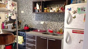 Eine Küche mit Herd, Backofen und Kühlschrank. Über der Arbeitsfläche befinden sich Regale mit verschiedenen Küchenutensilien.