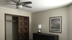 A hotel room with a bed, a desk with a lamp, a framed picture on the wall, and a closet with frosted glass panels. - Fully Renovated 2 Bed, 1 Bath Apartment near 8th Street (Saskatoon)