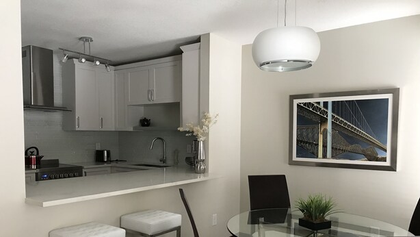 A modern kitchen with a built-in stove, a sink, and a dining area with a glass table and chairs. - Fully Renovated 2 Bed, 1 Bath Apartment near 8th Street (Saskatoon)