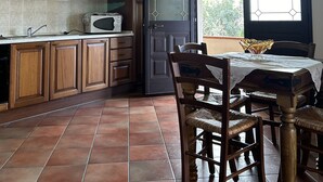 A kitchen with wooden cabinets, a tiled floor, and a dining area with a table and chairs. - Private Villa with Large Garden & Veranda – Relaxation & Comfort in Budoni (Budoni)
