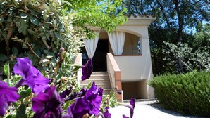 A building with a staircase leading to a door, surrounded by greenery and purple flowers. - Private Villa with Large Garden & Veranda – Relaxation & Comfort in Budoni (Budoni)