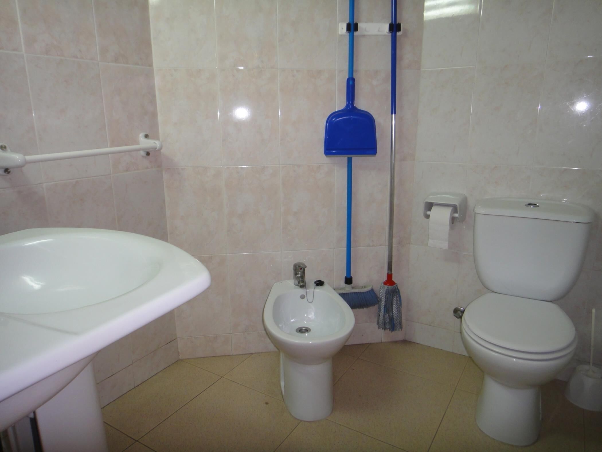 Une salle de bain avec un lavabo blanc, un bidet, des toilettes et des accessoires de nettoyage bleus.