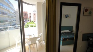 A balcony with a table and chairs, a bed with a blue headboard, and a view of buildings and greenery. - Apartments very close to the beach. Ref.LLORET SUN-24 (Lloret de Mar)