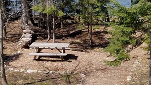 Una mesa de picnic en un área boscosa con árboles y suelo pedregoso.