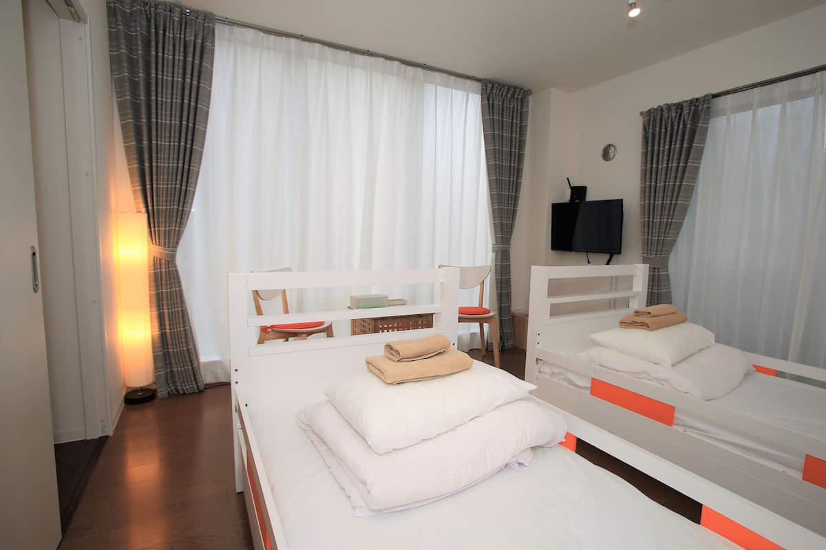 A hotel room with two single beds, a TV on the wall, and a window with curtains.