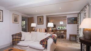 A living room with a sofa, coffee table, and lamps. There is a dining area with a table and chairs in the background.