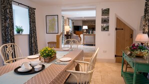 A dining area with a table set for four, chairs, a wooden cabinet, and a television in the background.