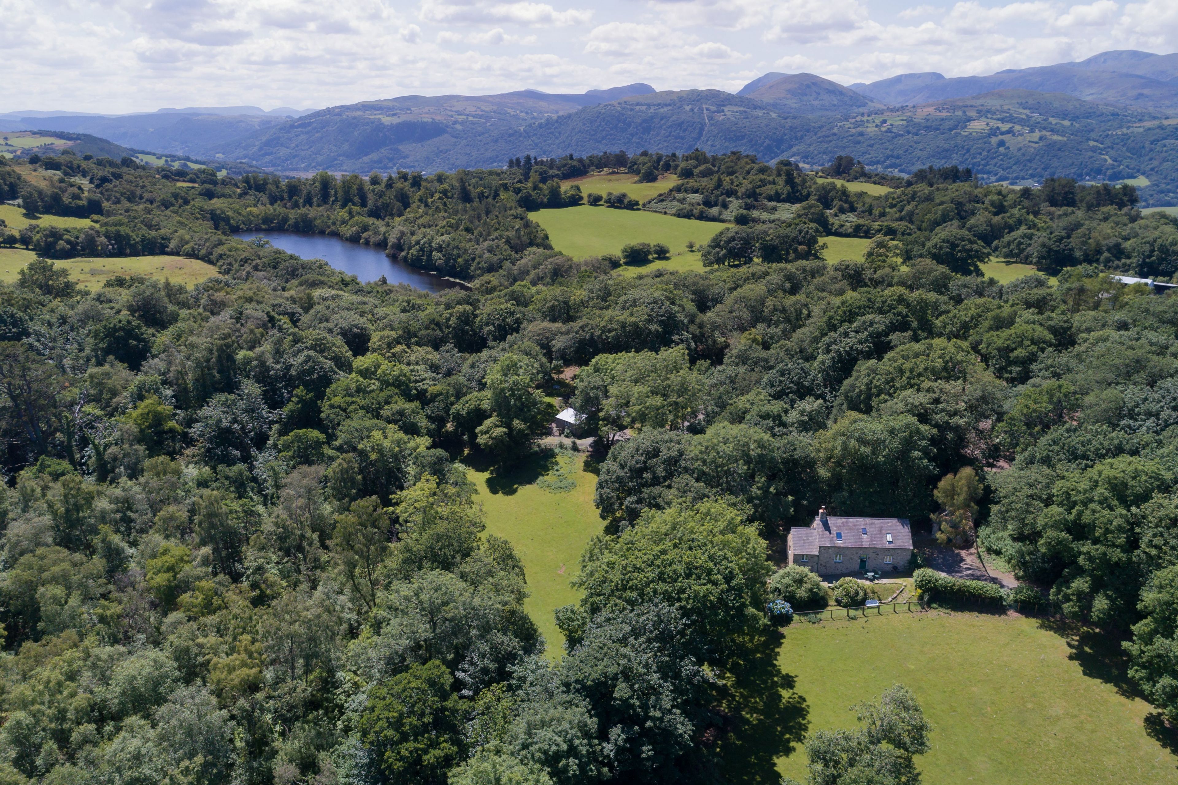A rural landscape with a lake, rolling hills, and a house surrounded by dense trees.