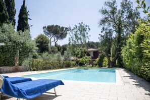 A swimming pool with lounge chairs, surrounded by greenery and a building in the background. - Villa with pool and beach access (Capoliveri)