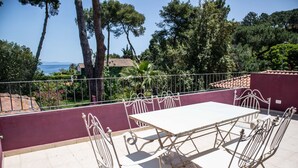 Une terrasse avec une table blanche et des chaises en métal, entourée d’un mur violet et d’une rambarde en métal.