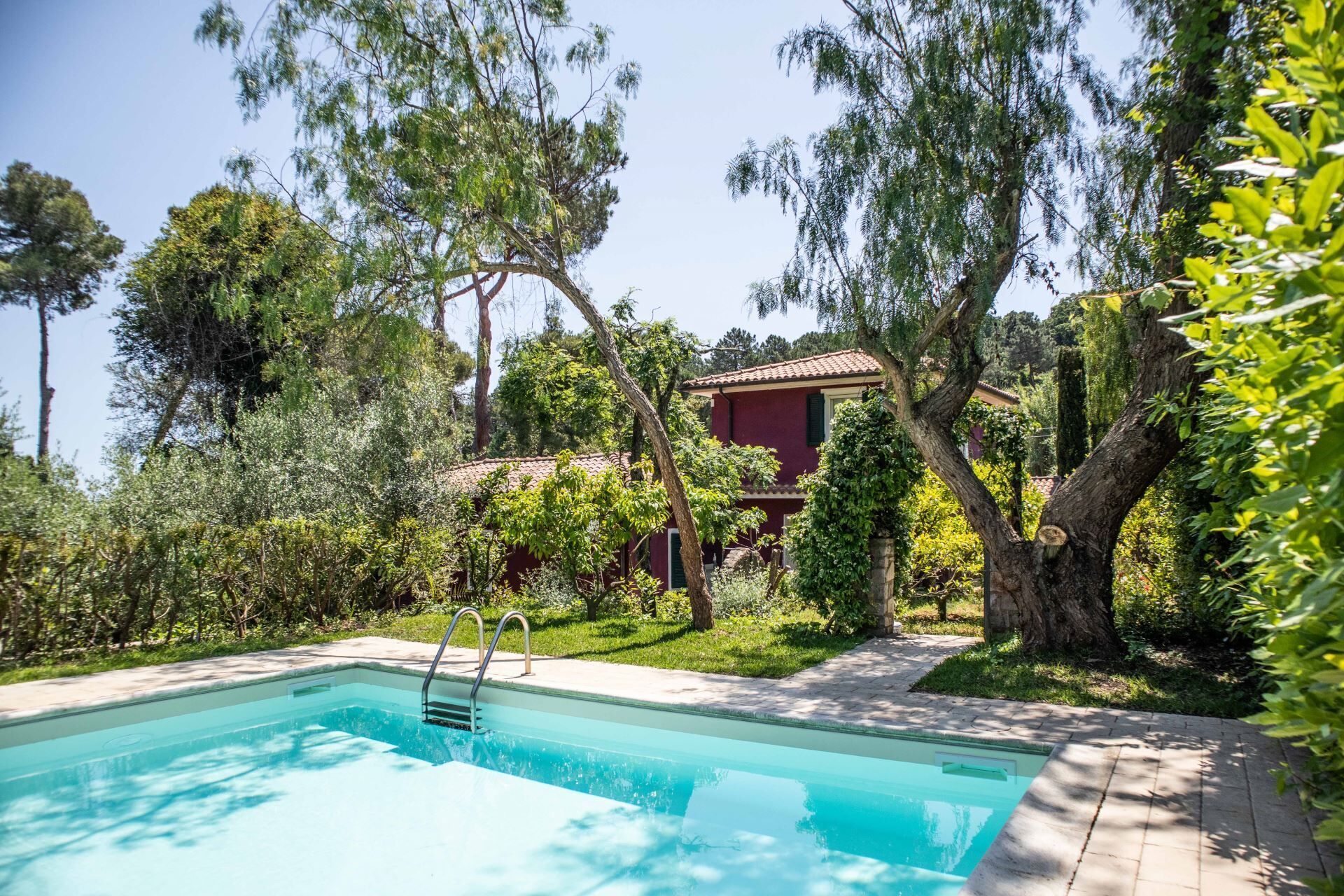 A swimming pool with a clear blue water surface, surrounded by lush greenery and trees.