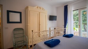 Une chambre à coucher comprenant un lit, une armoire, un téléviseur, une chaise et une vue sur la verdure par la fenêtre.
