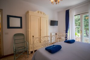 A bedroom with a bed, a wardrobe, a television, a chair, and a view of greenery through the window. - Villa with pool and beach access (Capoliveri)