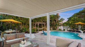 A covered outdoor area with a pool, seating, and tropical plants. - The Beach House | Southern Exposure | Walk or Bike to Vanderbilt Beach (Naples)
