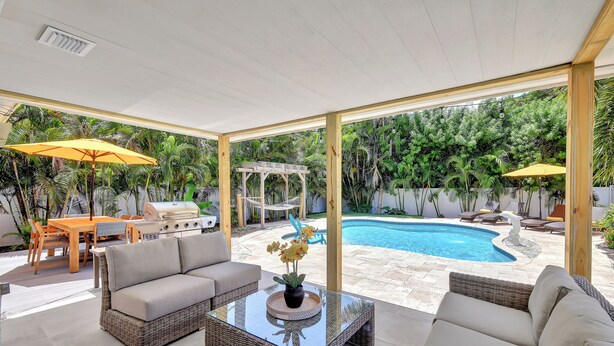 A spacious outdoor area with a pool, wicker furniture, and yellow umbrellas. - The Beach House | Southern Exposure | Walk or Bike to Vanderbilt Beach (Naples)