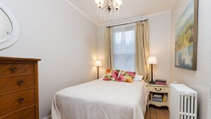 A bedroom with a bed, a dresser, a nightstand, a radiator, and a painting on the wall. - Unit 2, 1st floor 1 Bdrm, walk to mansion and beach (Newport)