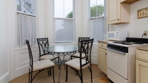 A kitchen with a round glass table, four chairs, a stove, a microwave, and a window with a view of trees. - Unit 2, 1st floor 1 Bdrm, walk to mansion and beach (Newport)