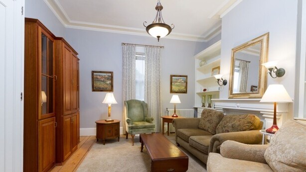 A living room with a wooden cabinet, green armchair, beige sofa, and a fireplace with a mirror above it. - Unit 2, 1st floor 1 Bdrm, walk to mansion and beach (Newport)