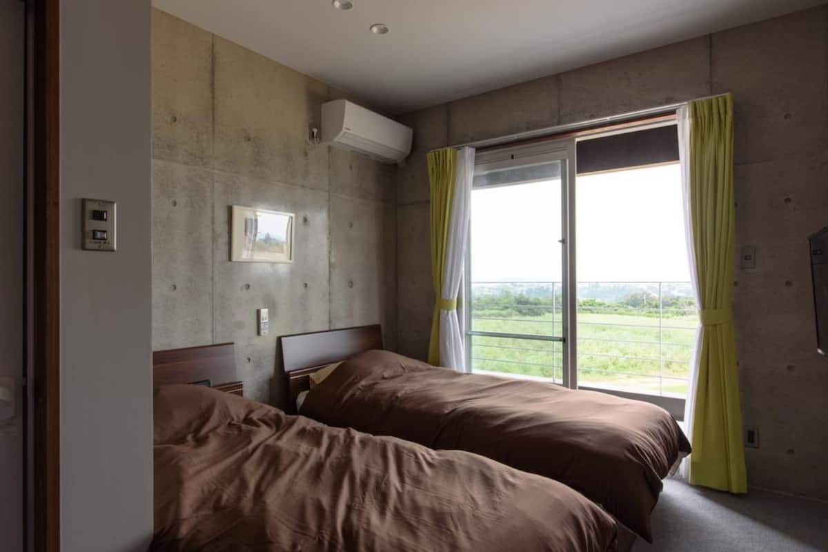 A bedroom with two beds, a window with curtains, an air conditioning unit, and a view of the outdoors.