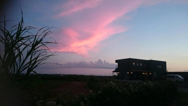 Un edificio de techo plano y balcón, ubicado cerca de una masa de agua con un cielo rosado al fondo.