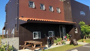 Un edificio moderno con fachada marrón, múltiples ventanas y un área de estar exterior cubierta.