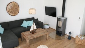 A modern living room with a dark grey sofa, a wooden coffee table, a small sailboat model, a round woven rug, a wall-mounted TV, a wood-burning stove, and a lantern. - HOUSE ON THE LAKE WITH DIRECT ACCESS TO THE LAKE (Frymburk nad Vltavou)