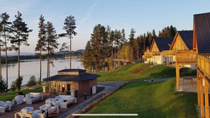 Un hotel frente al lago con cabañas de madera, un edificio central con fachada de vidrio y zonas de estar al aire libre.
