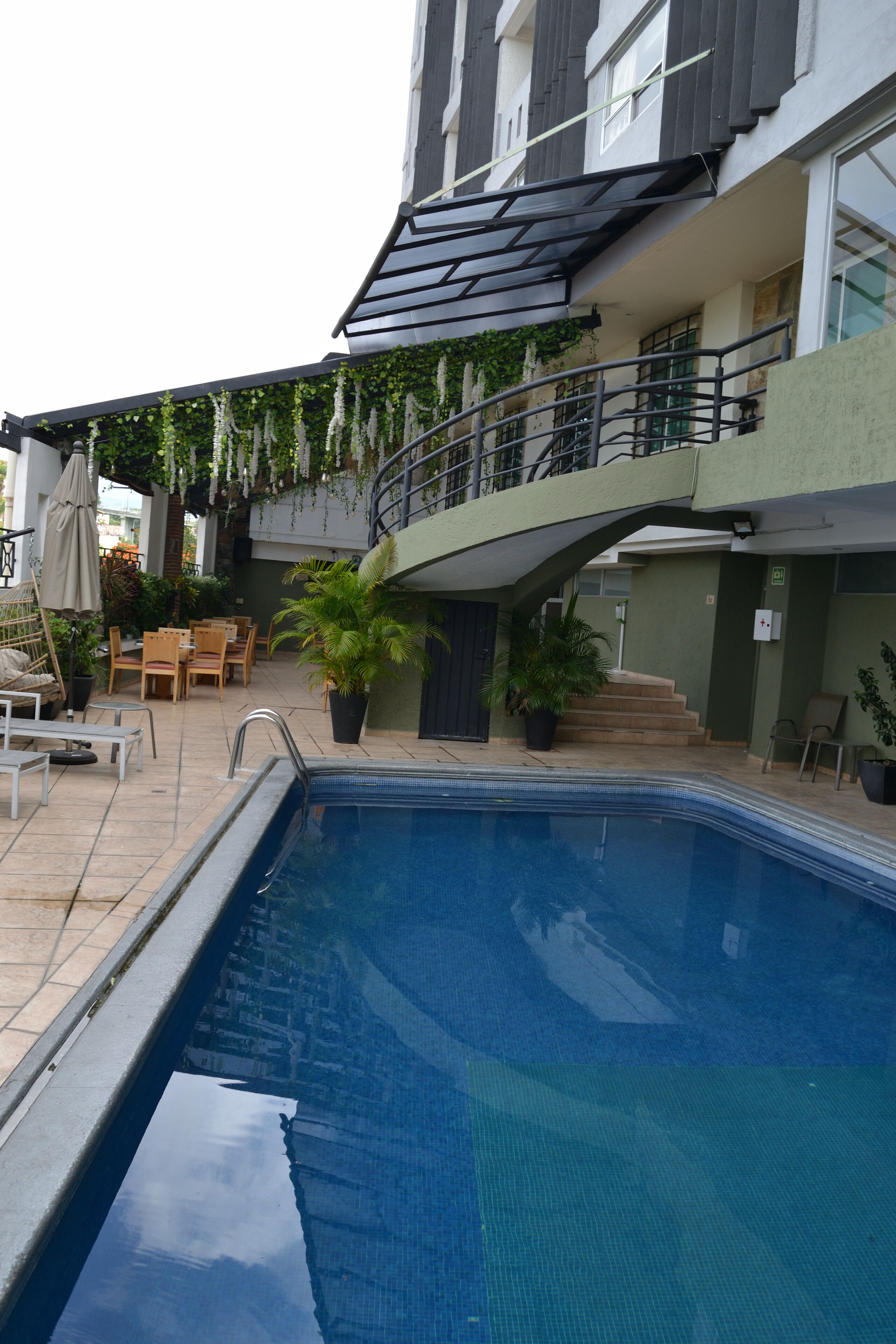 A swimming pool with a sunshade, outdoor seating, and potted plants.