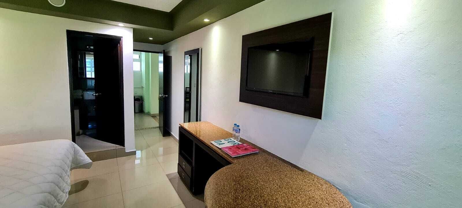 A hotel room with a bed, a small desk with a water bottle, and a TV mounted on the wall.