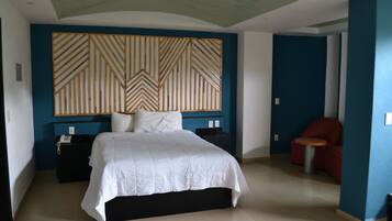 Habitación de hotel con una cama grande, cabecero de madera, una mesita y una silla roja.
