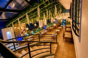 Un restaurante con una escalera, plantas de interior, luces colgantes y varias mesas de comedor.