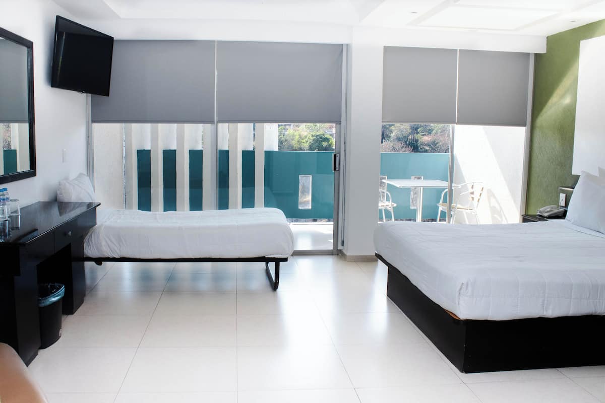 A hotel room with two beds, a desk, a TV, and a balcony with a view.