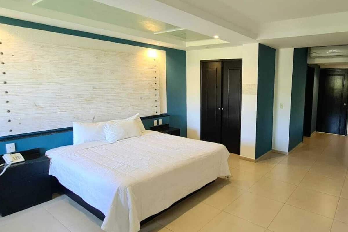A hotel room with a bed, a desk with a chair, a TV, and a door leading to another room.