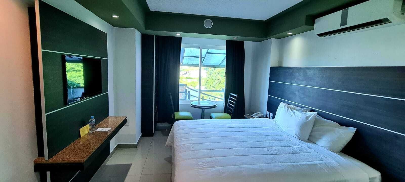 A hotel room with a large bed, a desk, a chair, and a balcony with a table and chairs.