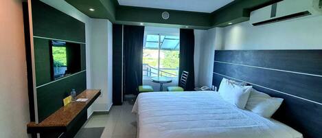 A hotel room with a large bed, a desk, a chair, and a balcony with a table and chairs.