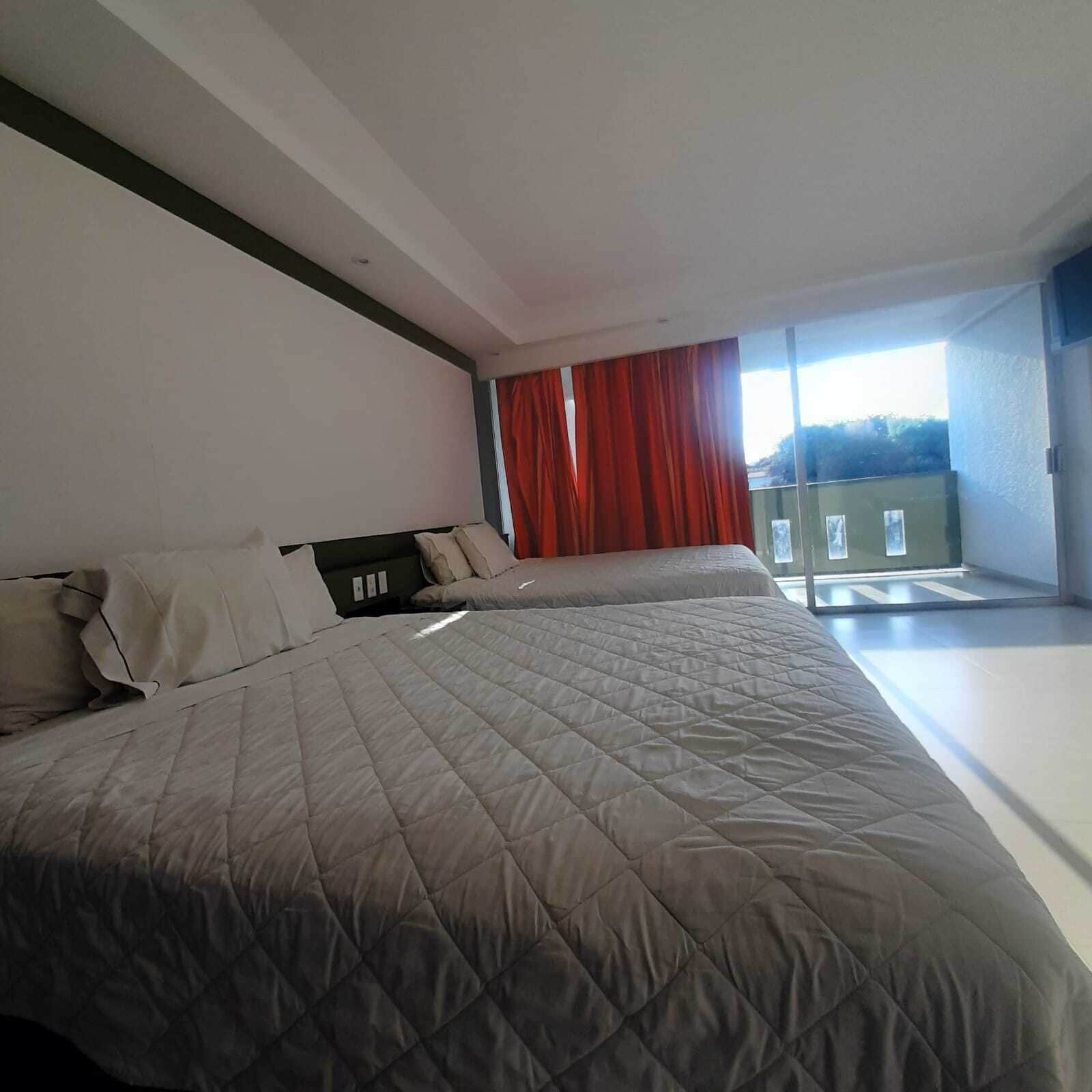 A modern hotel room with two beds, a large window with red curtains, and a balcony.