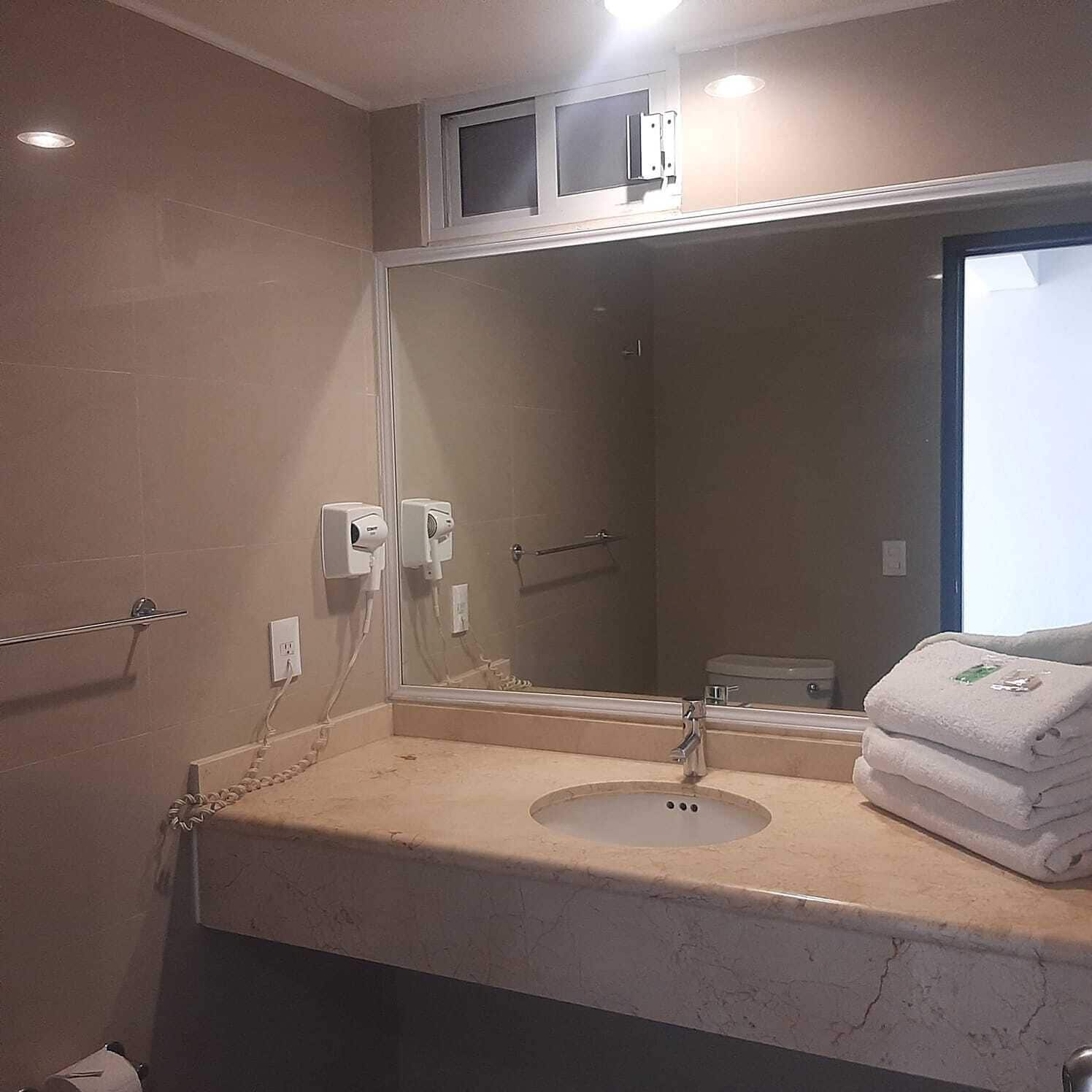A bathroom with a sink, mirror, towel rack, and a towel stack.