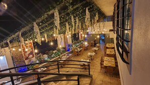 Un restaurant interior amb una escala que condueix a una zona de dinar, decorat amb plantes penjants i llums de cadena.